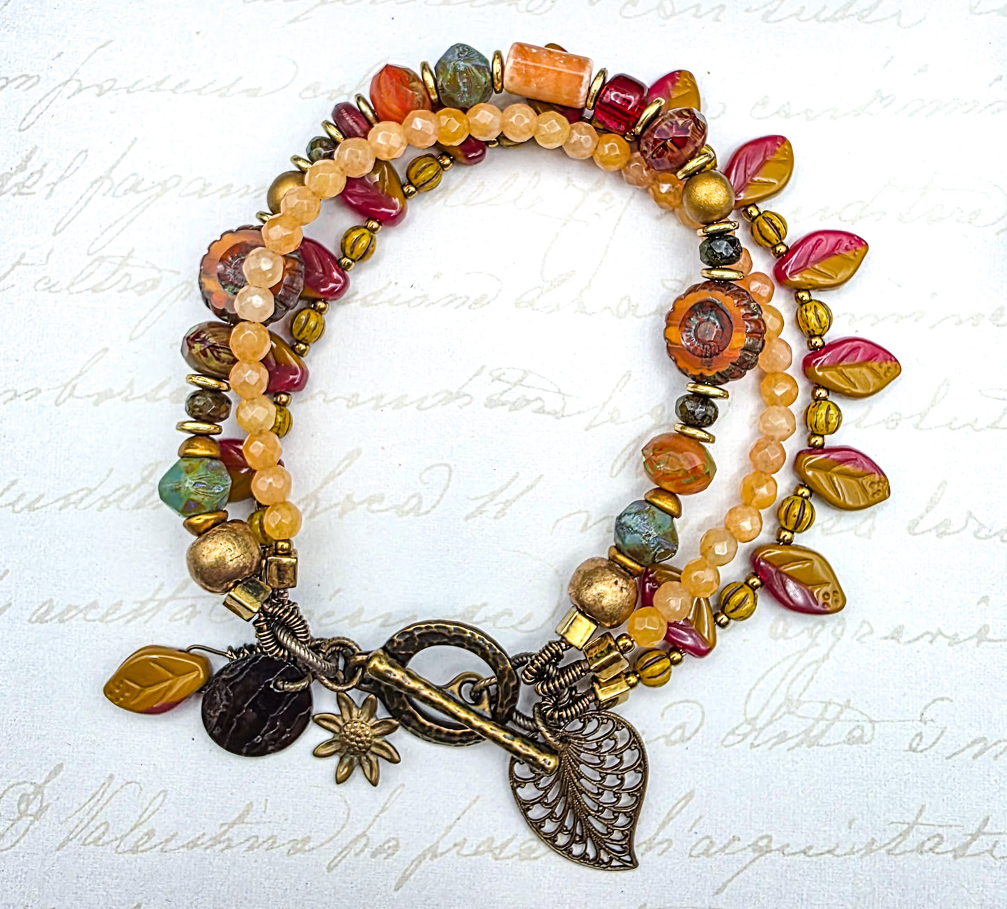 Colorful beaded bracelet with leaf charms on a textured white background