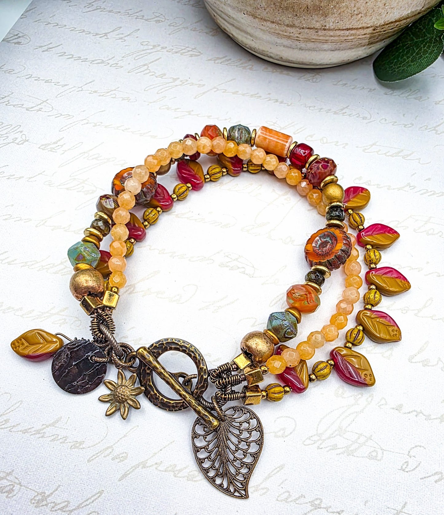 Multicolored beaded bracelet with leaf charms on a textured surface