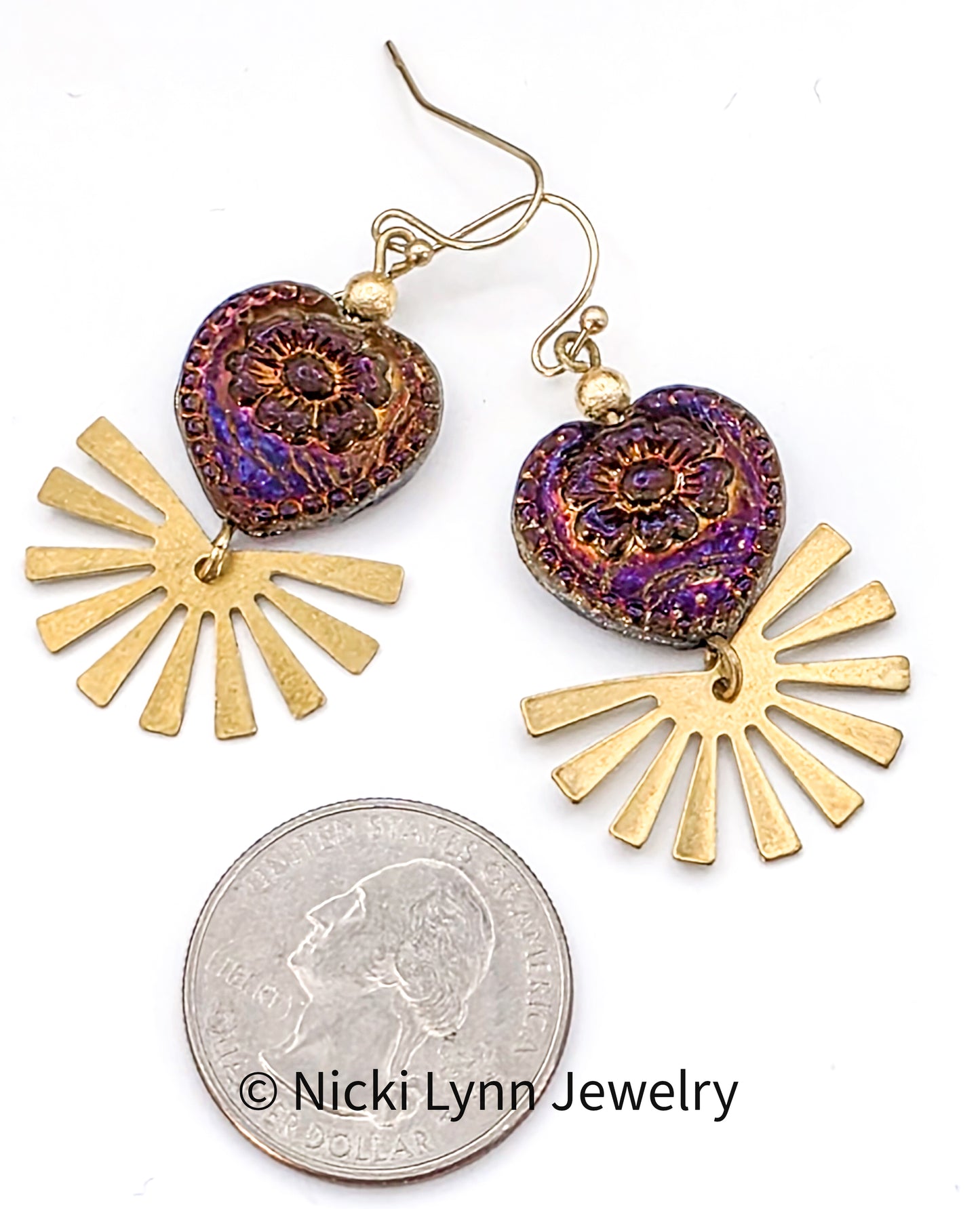 Gold and purple heart-shaped earrings with sunburst designs on a white background, shown next to a quarter for scale.