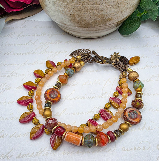 Multicolored beaded bracelet with leaf charms on a textured surface