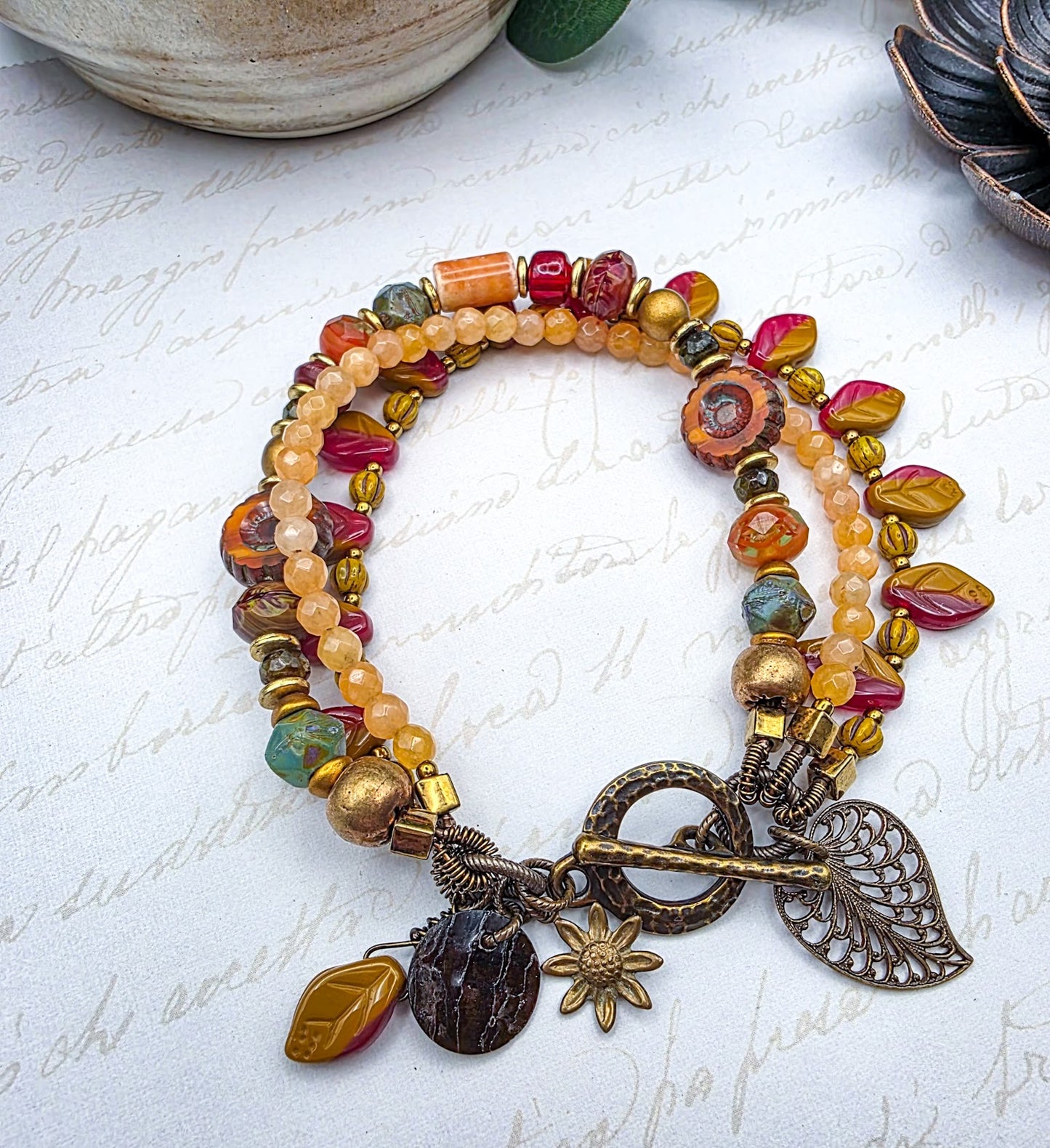 Multicolored beaded bracelet with leaf and sunflower charms on a textured white surface.