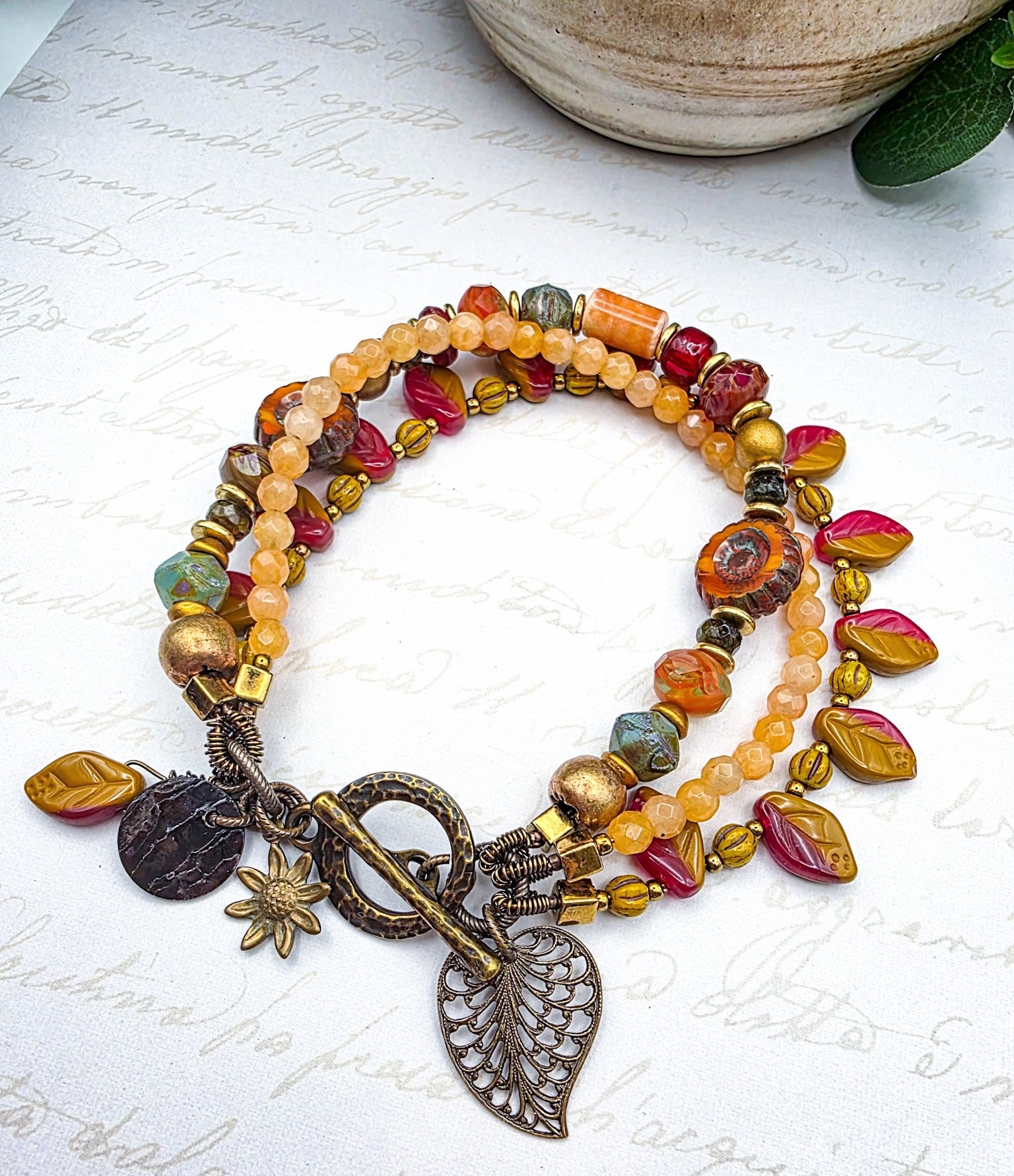 Multicolored beaded bracelet with leaf charms on a textured surface