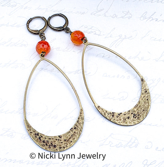 Gold hoop earrings with orange beads on a textured white background, featuring Nicki Lynn Jewelry branding.
